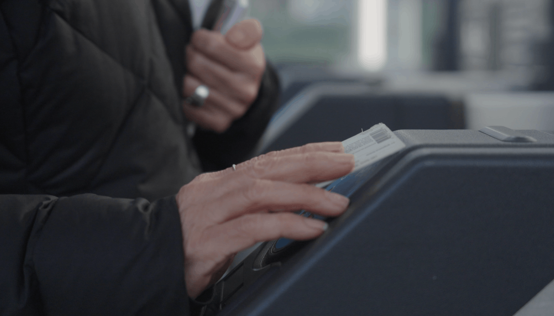 A person's hands tapping a subway card on a turnstile.